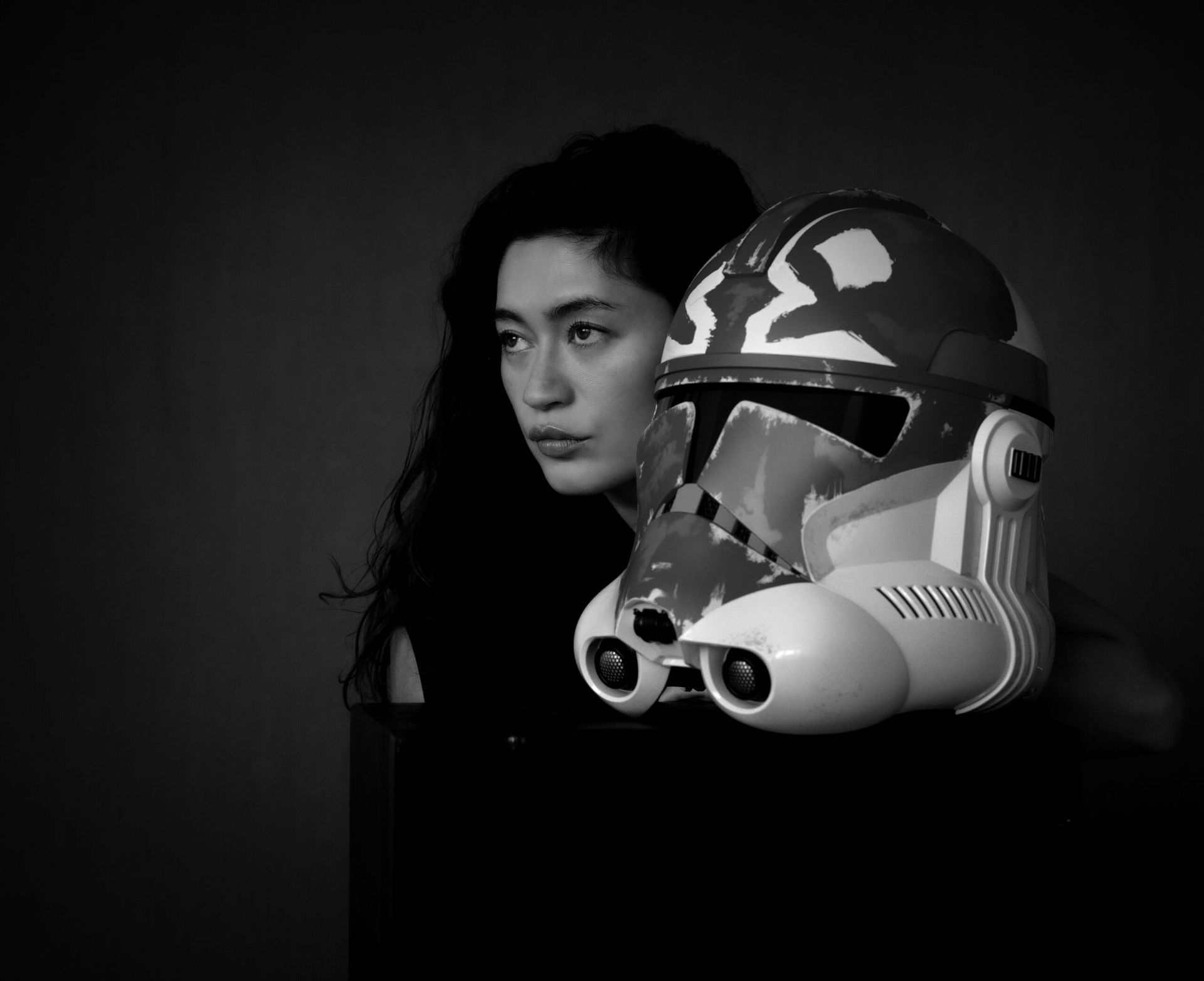 Une femme regarde à gauche, un casque de soldat clone à côté d'elle. Photo en noir et blanc.