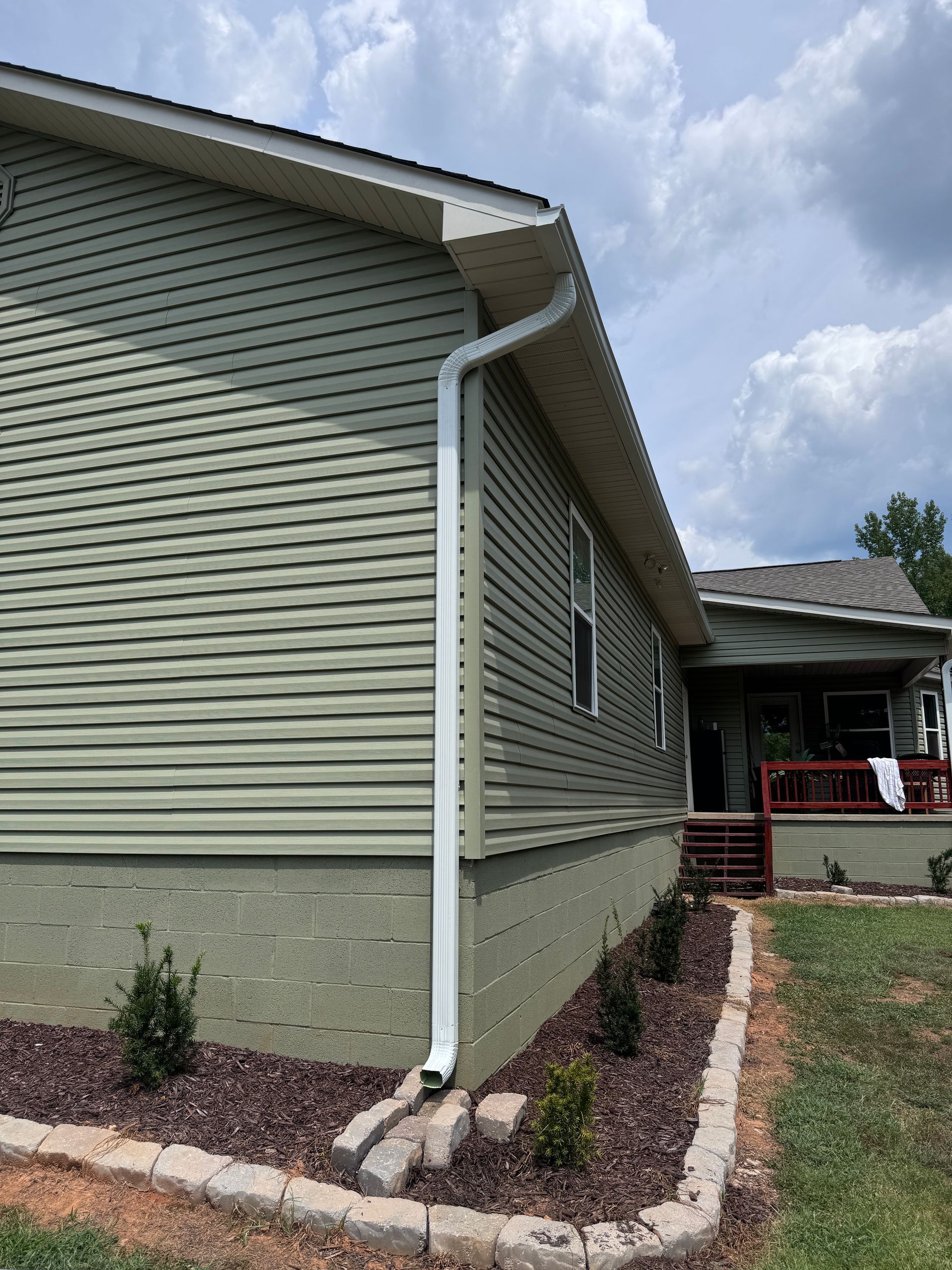 A green house with a white gutter on the side of it.