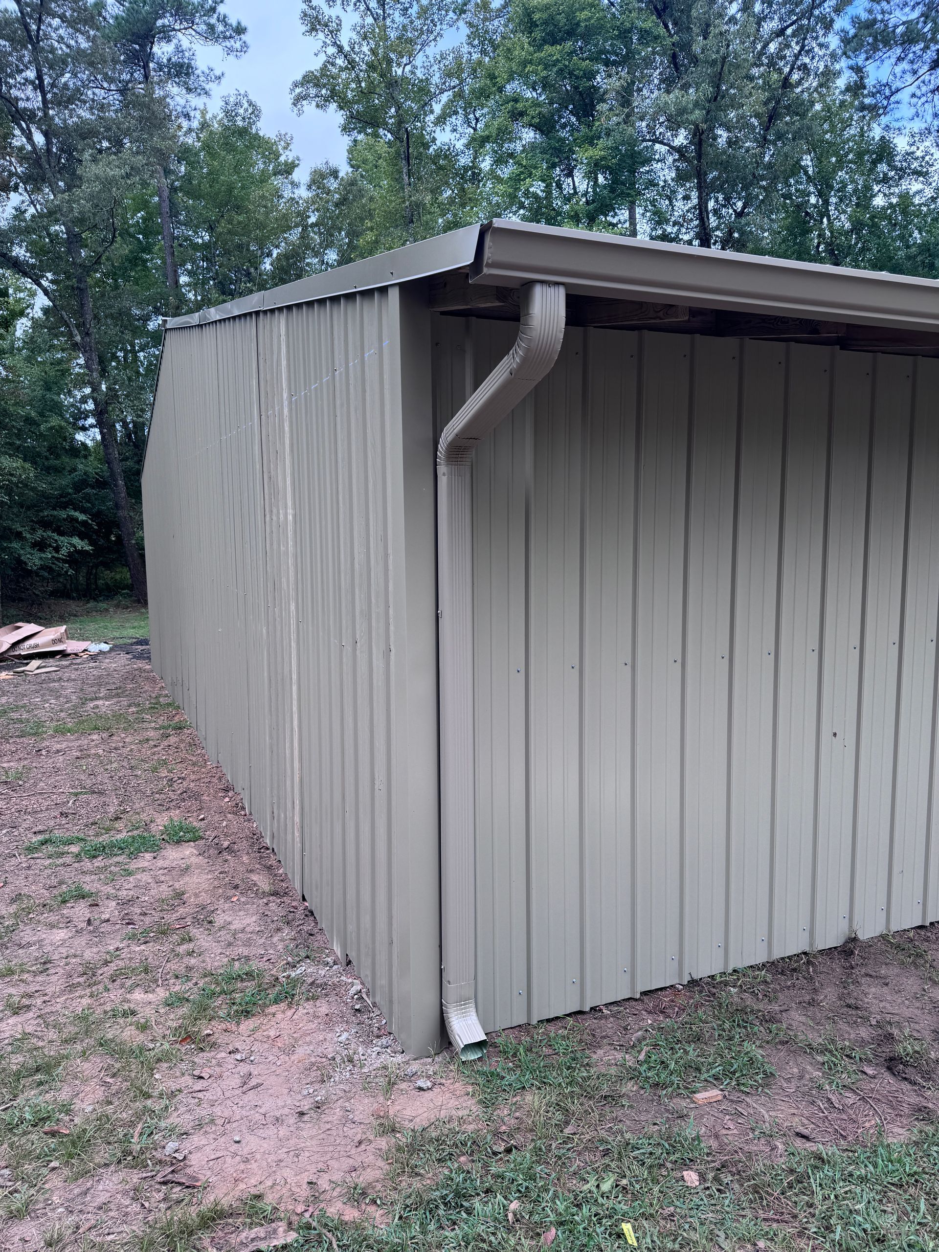 A shed with a gutter on the side of it is sitting in the middle of a grassy field.