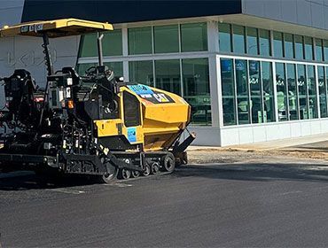 A Yellow And Black Asphalt Paving Machine Is Parked In Front Of A Building — Elite Bitumen & Asphalt In Mackay, QLD
