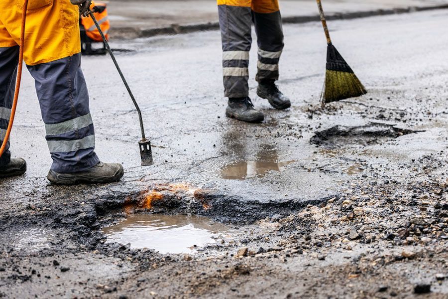 A Man Is Using a Broom to Clean a Pothole in The Road — Elite Bitumen & Asphalt In Mackay, QLD