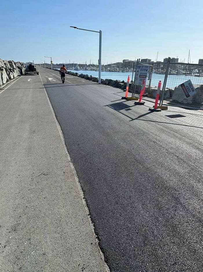 A Person Is Riding A Bike Down A Road Next To A Body Of Water — Elite Bitumen & Asphalt In Mackay, QLD