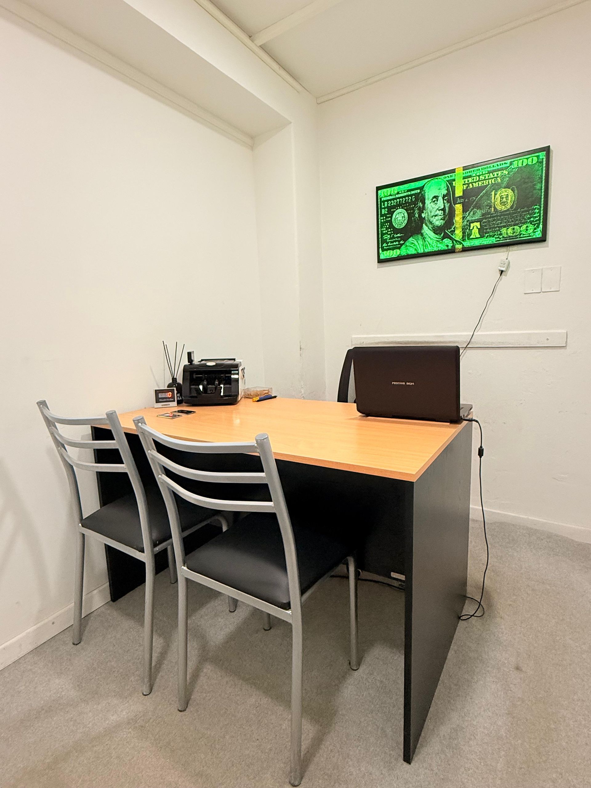 Una habitación con un escritorio, sillas y una computadora portátil encima.