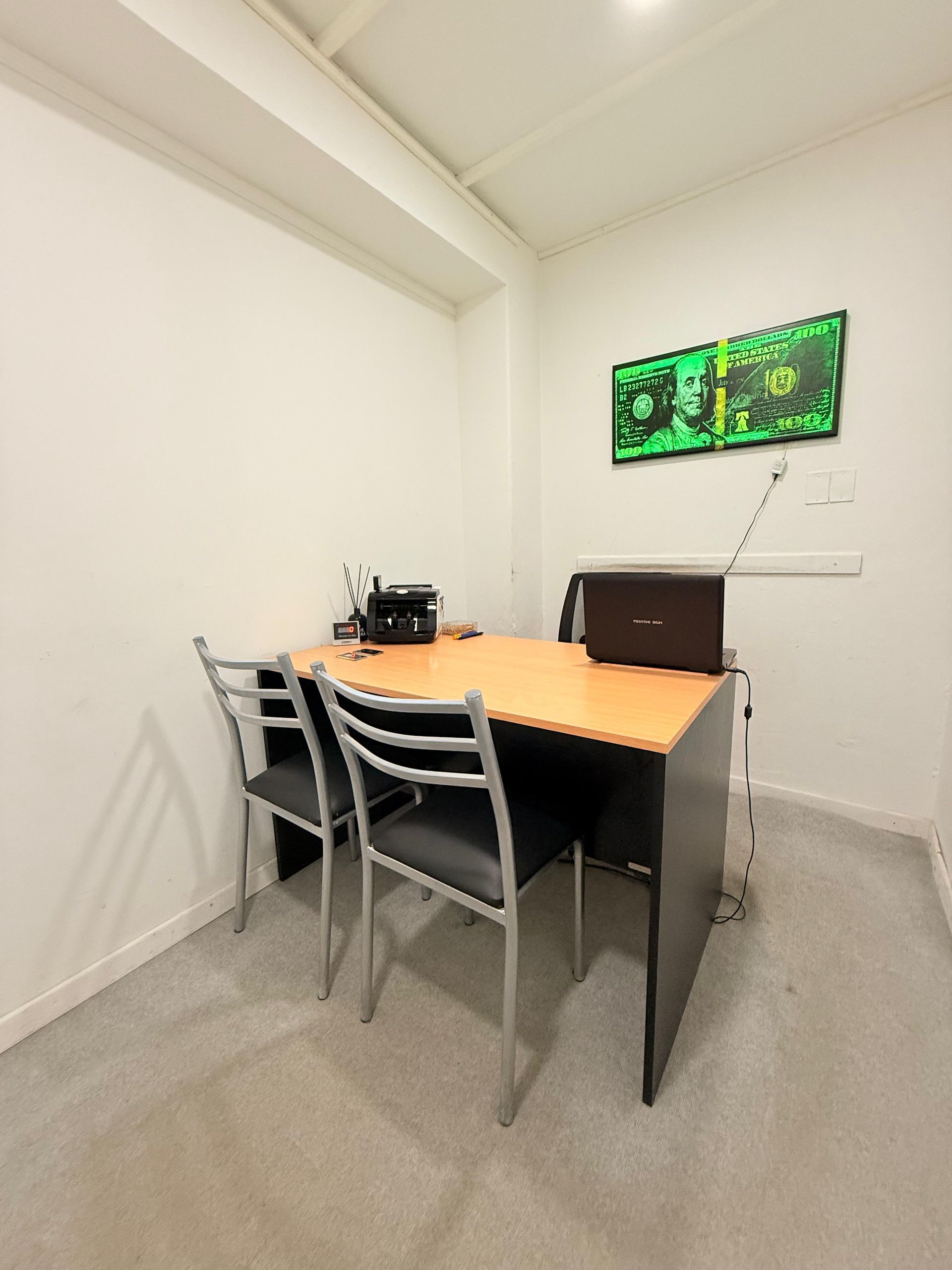 Una pequeña oficina con un escritorio, sillas y una computadora portátil.