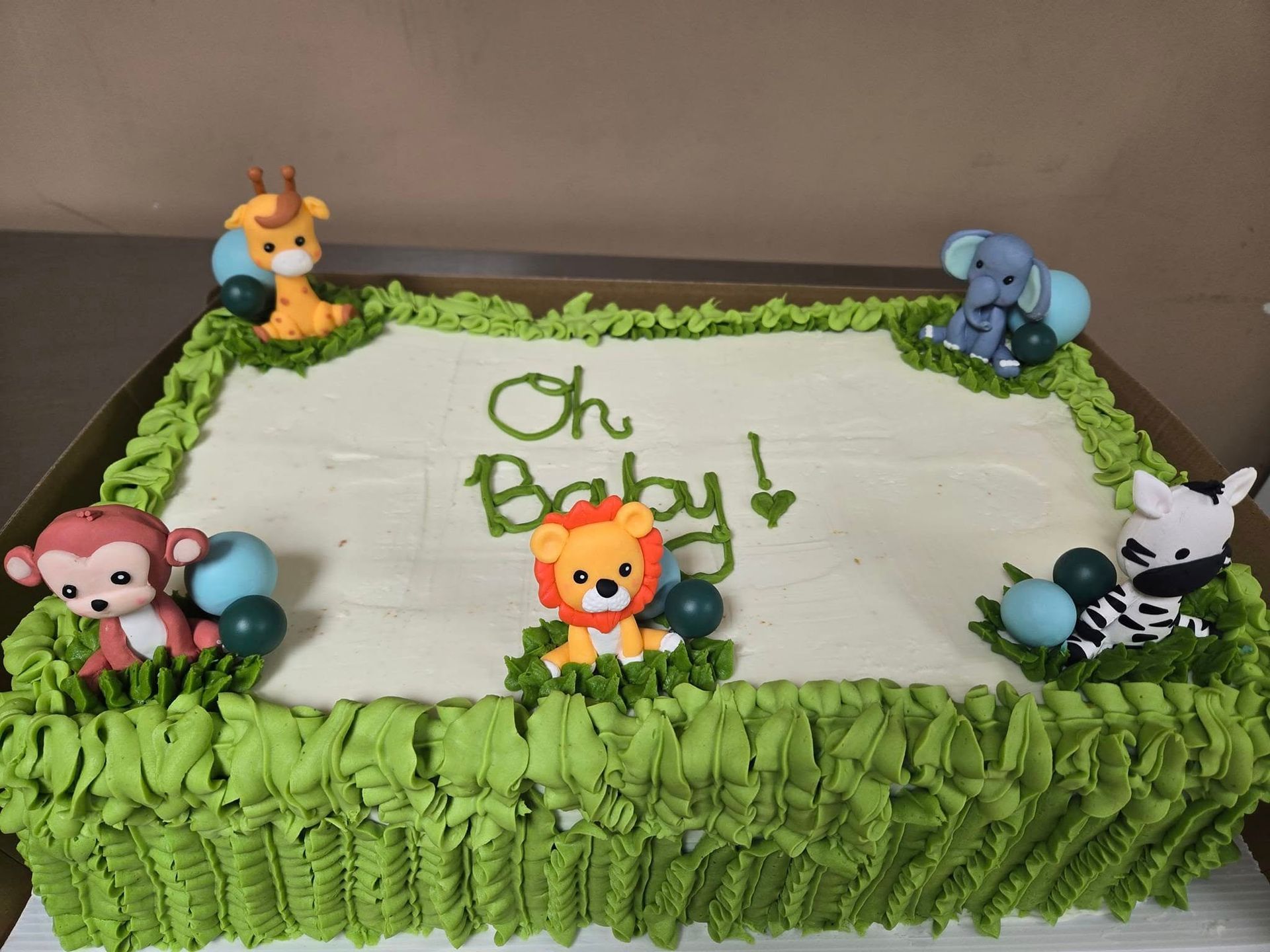Decorated cake with white frosting, green grass border, and jungle animals around “Oh Baby” text.