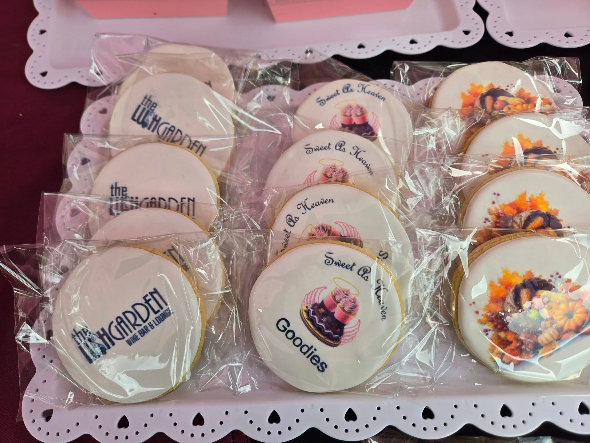 Assorted decorated round cookies in clear bags, displayed on a white tray with lace edging.