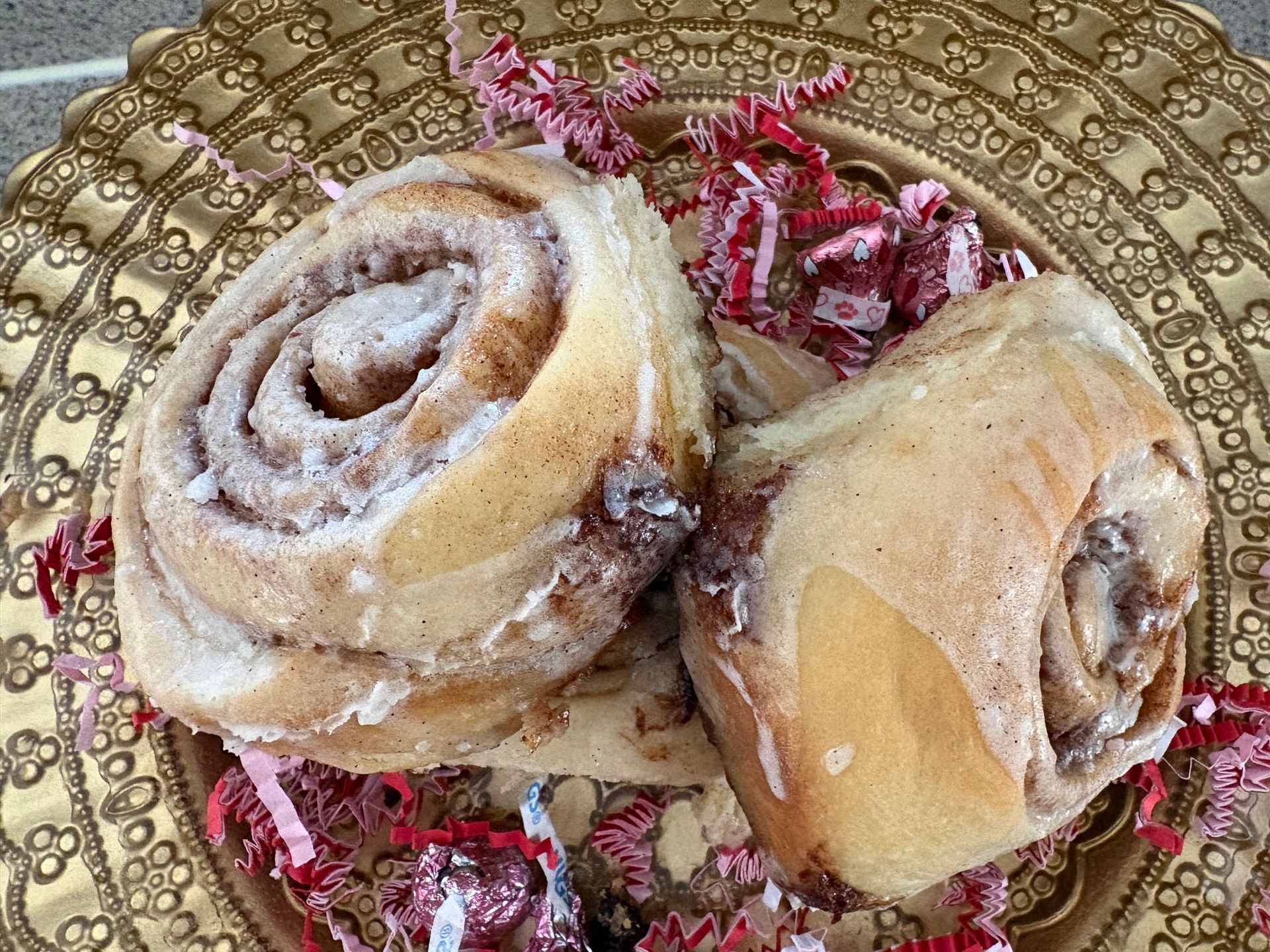 Two powdered cinnamon rolls on a decorative gold plate with pink shredded garnish