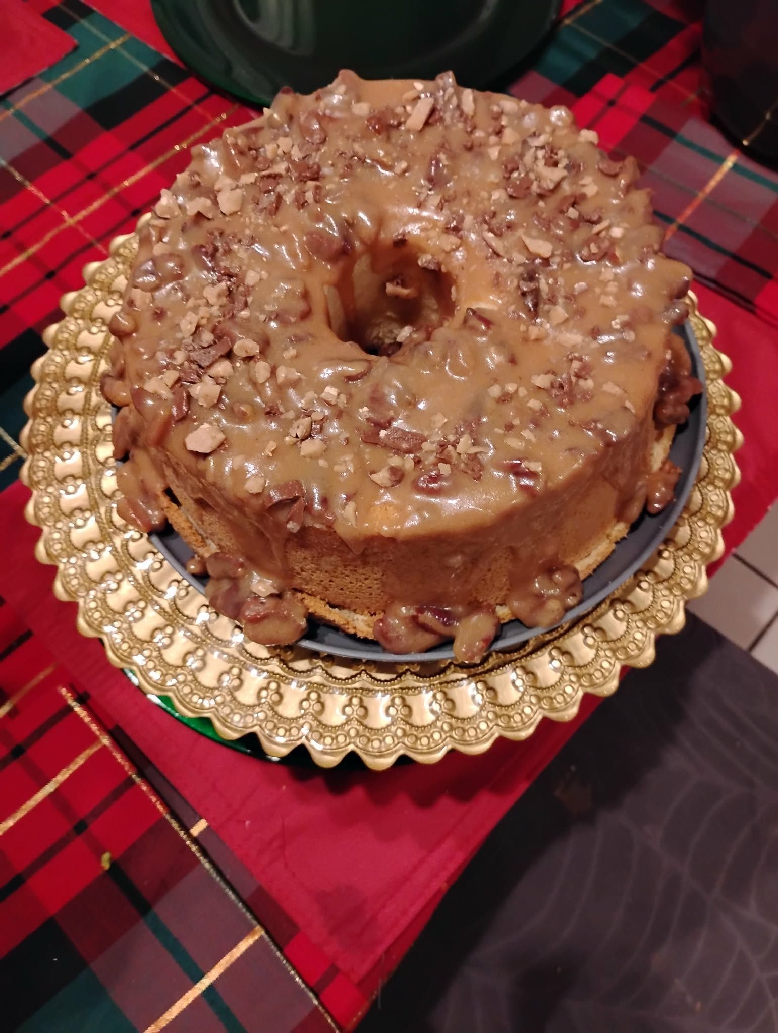 Round caramel-glazed bundt cake with nuts on a gold platter over a red plaid tablecloth