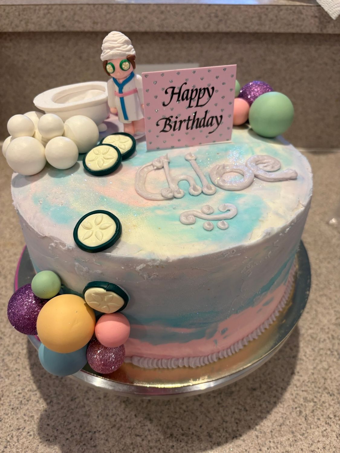 Pastel birthday cake with rainbow frosting, fruit slices, and a “Happy Birthday” topper on a table
