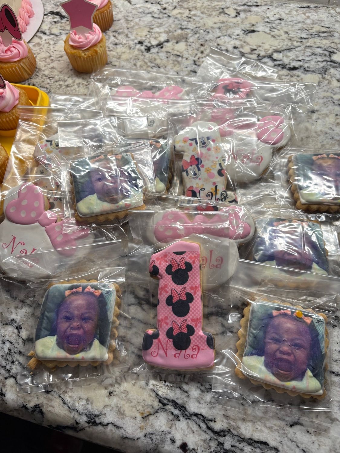 Assorted decorated mini dessert treats on a granite countertop, some with pink and purple icing and photo toppers