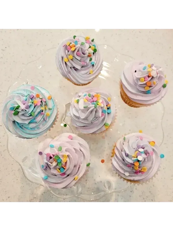 Six pastel-frosted cupcakes with colorful sprinkles on a white tray
