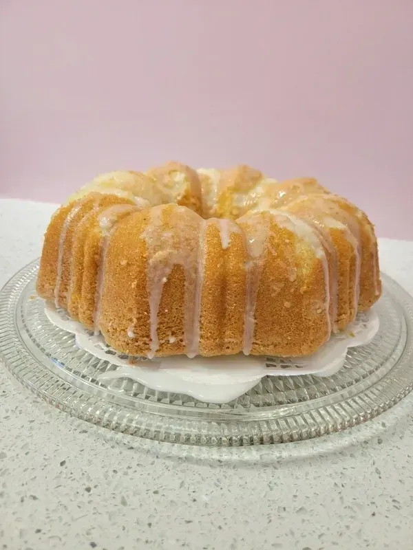 Glazed bundt cake on a glass plate against a pale pink background