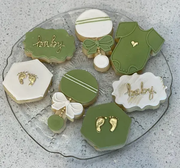 Tray of green and white baby-themed decorated cookies with bows, footprints, and “baby” icing.