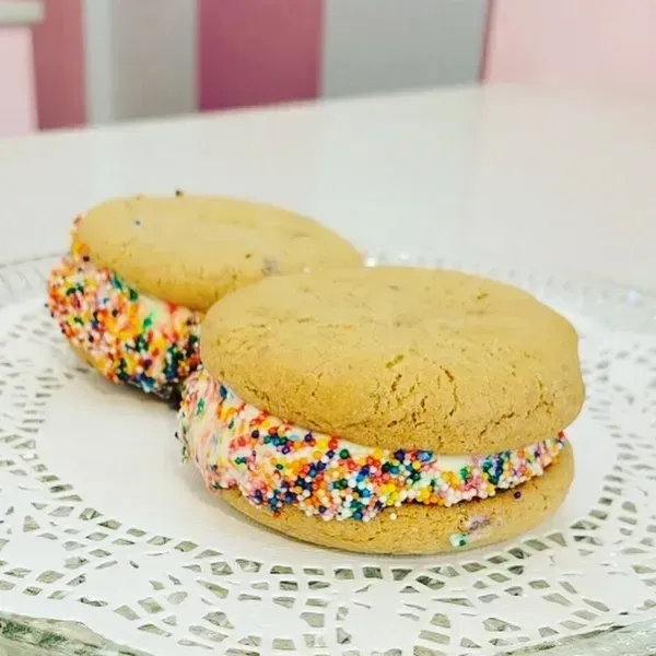 Two sprinkle-filled sandwich cookies on a white doily, one in front of the other.