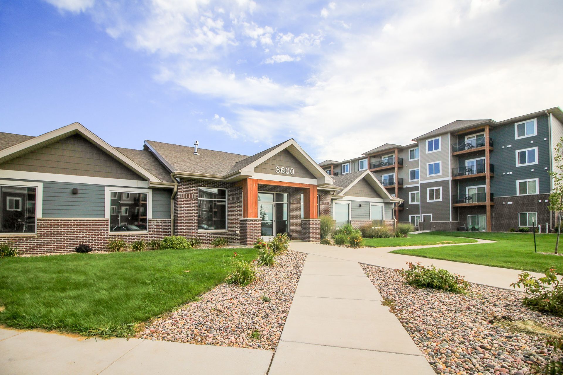 Apartment complex with a stone and blue facade and an adjacent multi-story building.  A walkway leads to the entrance under a partly cloudy sky.