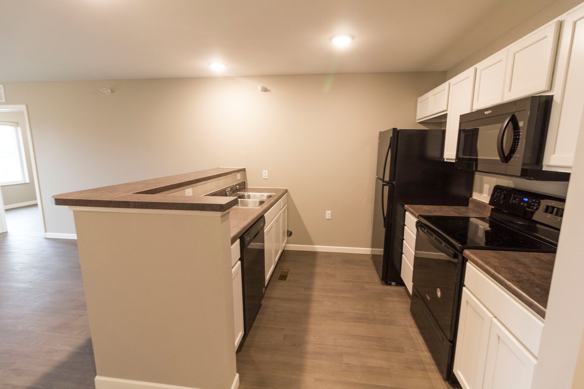 Kitchen with white cabinets, black appliances, and a breakfast bar with a brown countertop. Light brown flooring, neutral walls.
