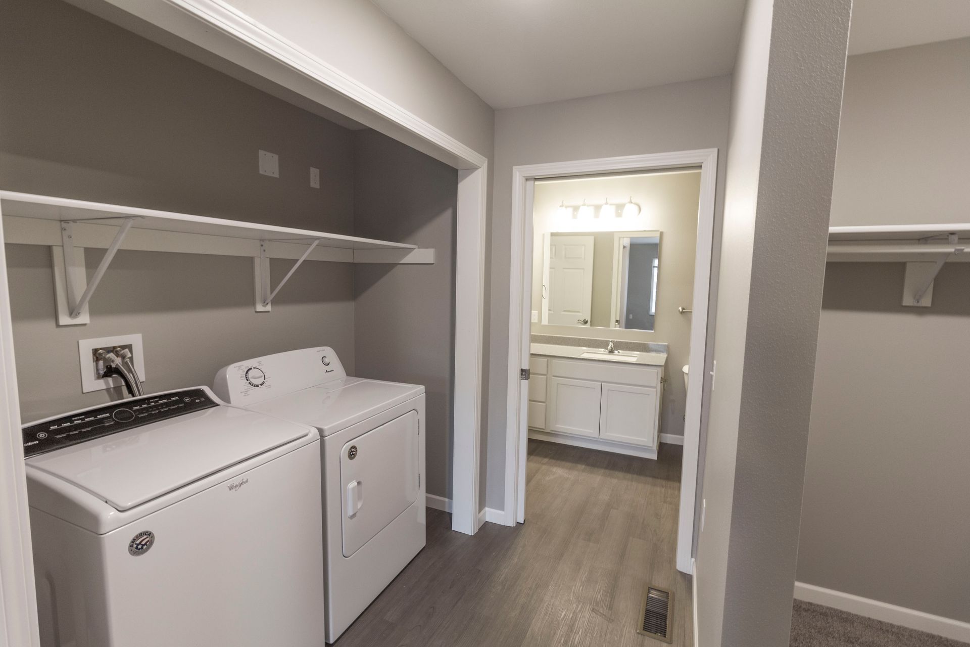 Laundry room with washer and dryer, open shelving, and a doorway leading to a bathroom with a white vanity.