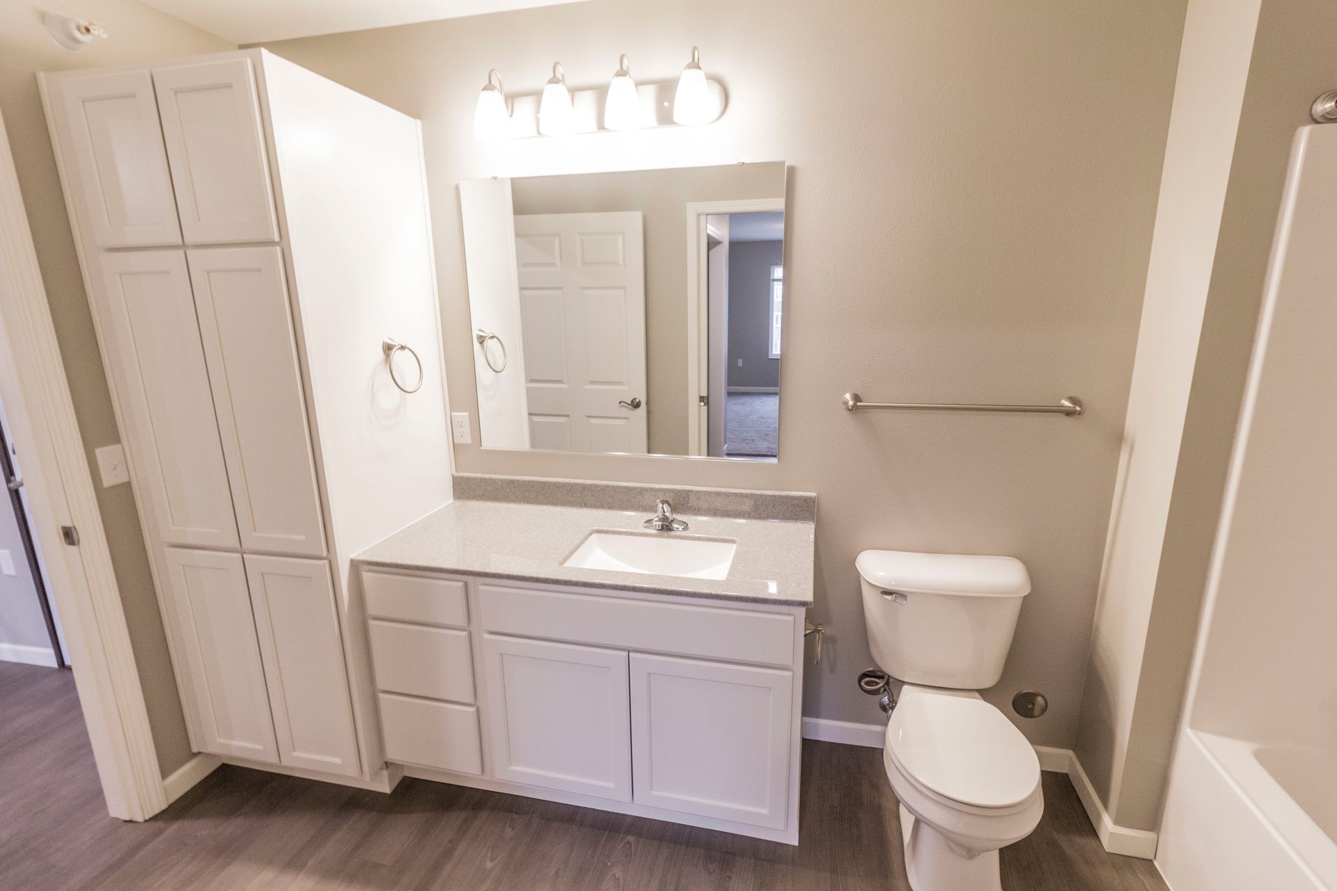 Bathroom with white cabinets, gray countertop and walls, toilet, and tall storage cabinet.