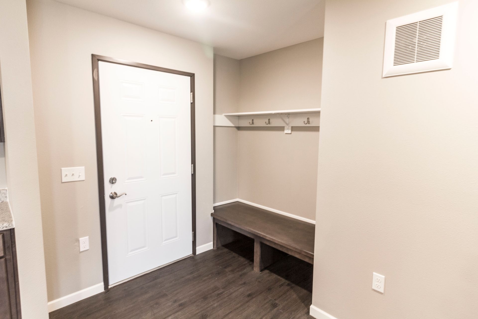 Entryway with a white door, built-in bench, coat rack, and dark wood flooring, painted in neutral tones.