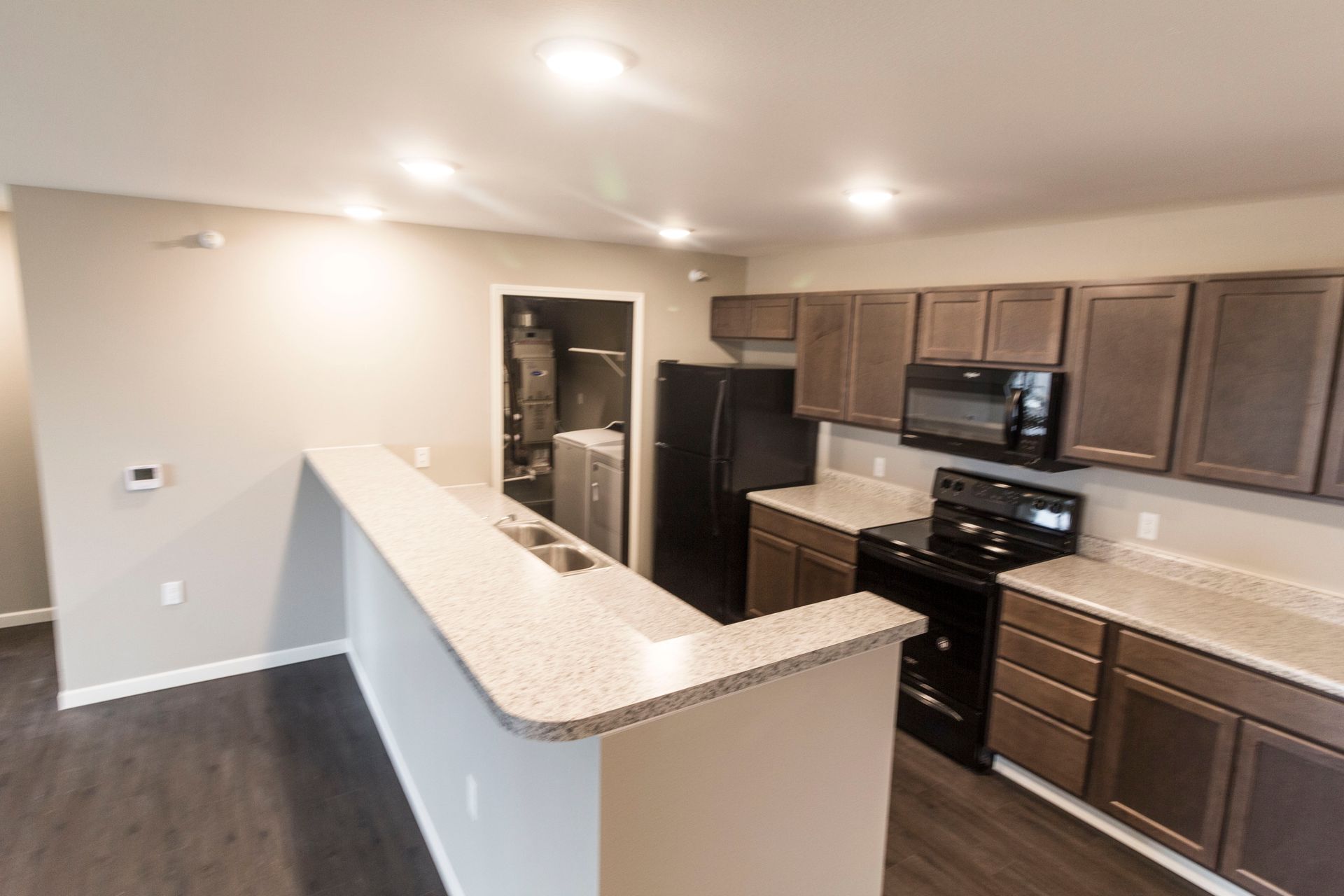 Kitchen with brown cabinets, black appliances, and a countertop bar. Dark flooring and a laundry area are visible.