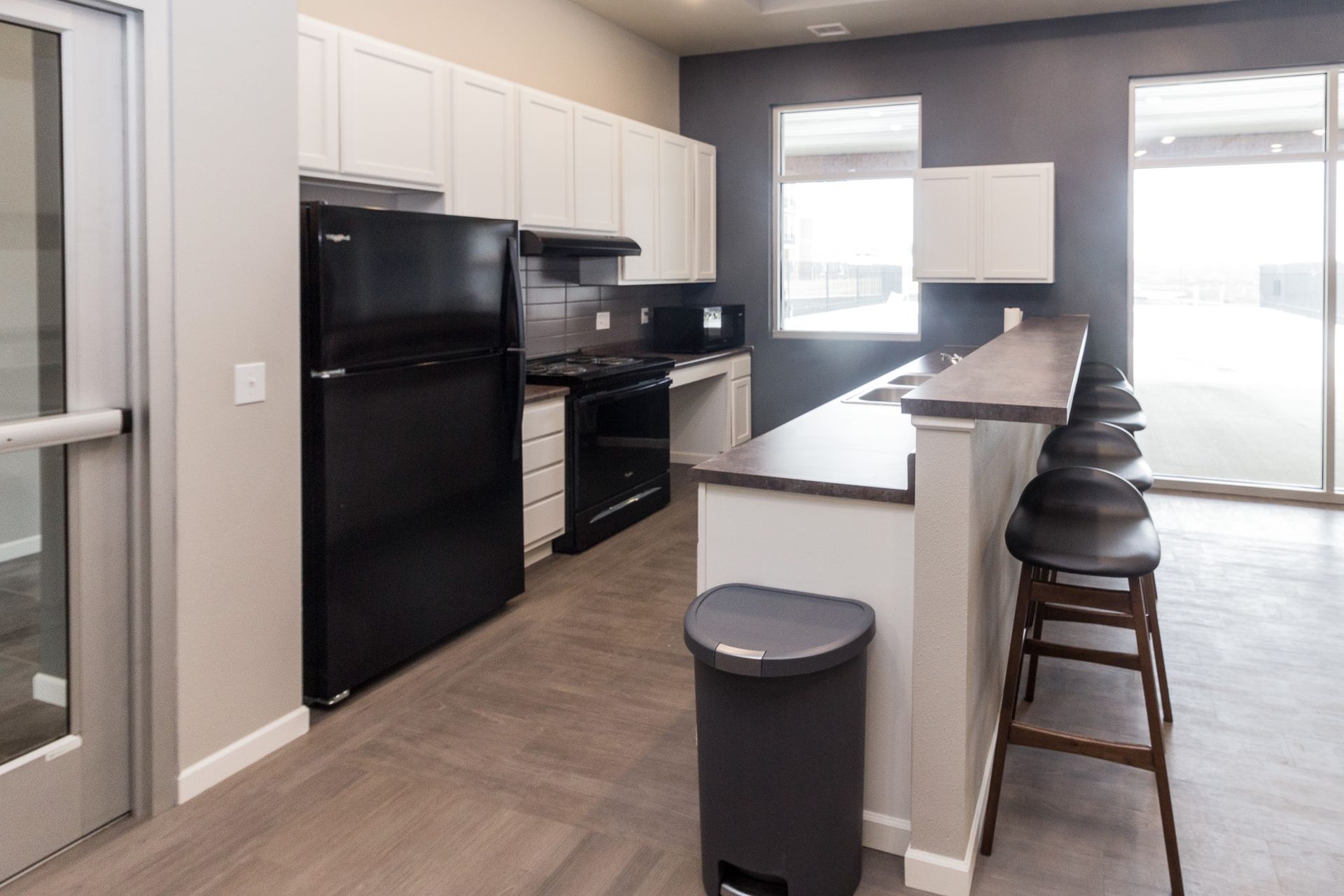 Kitchen with white cabinets, black appliances, a bar counter, and a gray trash can.