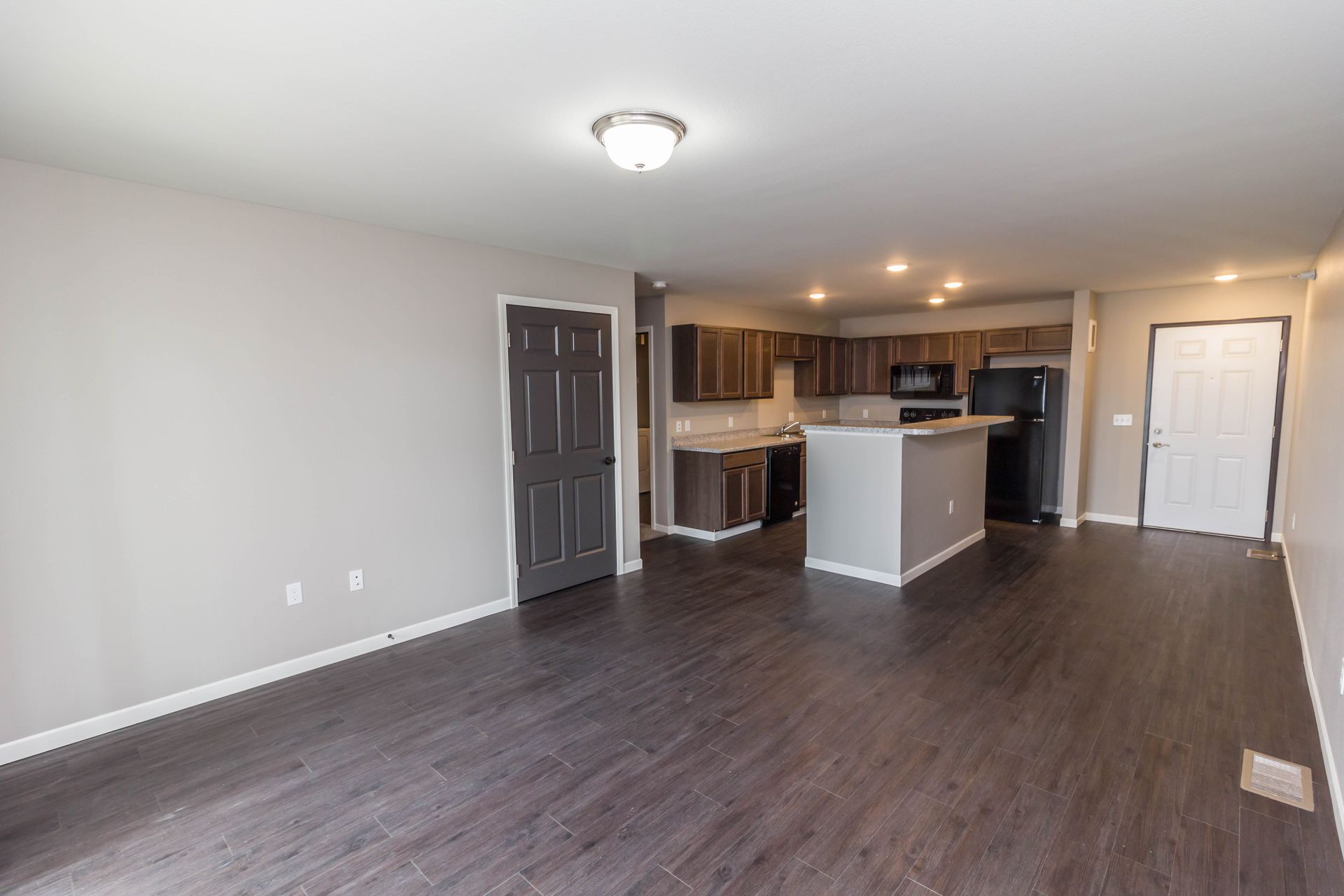Open-concept living space with a kitchen and island. Dark wood-look flooring, gray walls, and dark brown kitchen cabinets.