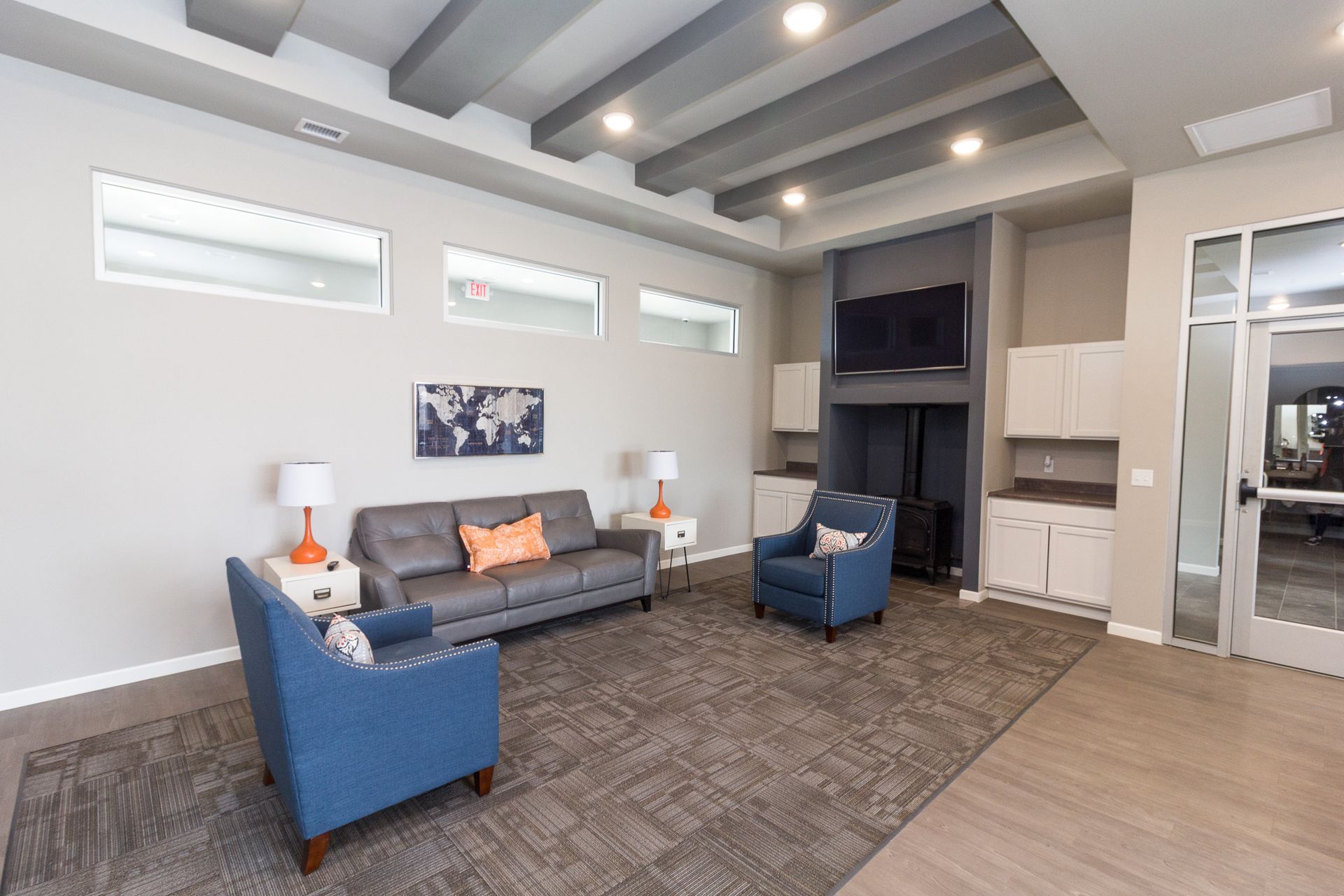 Lounge area with gray walls, gray ceiling beams, and blue furniture. Features a sofa, armchairs, TV, and a map art piece.