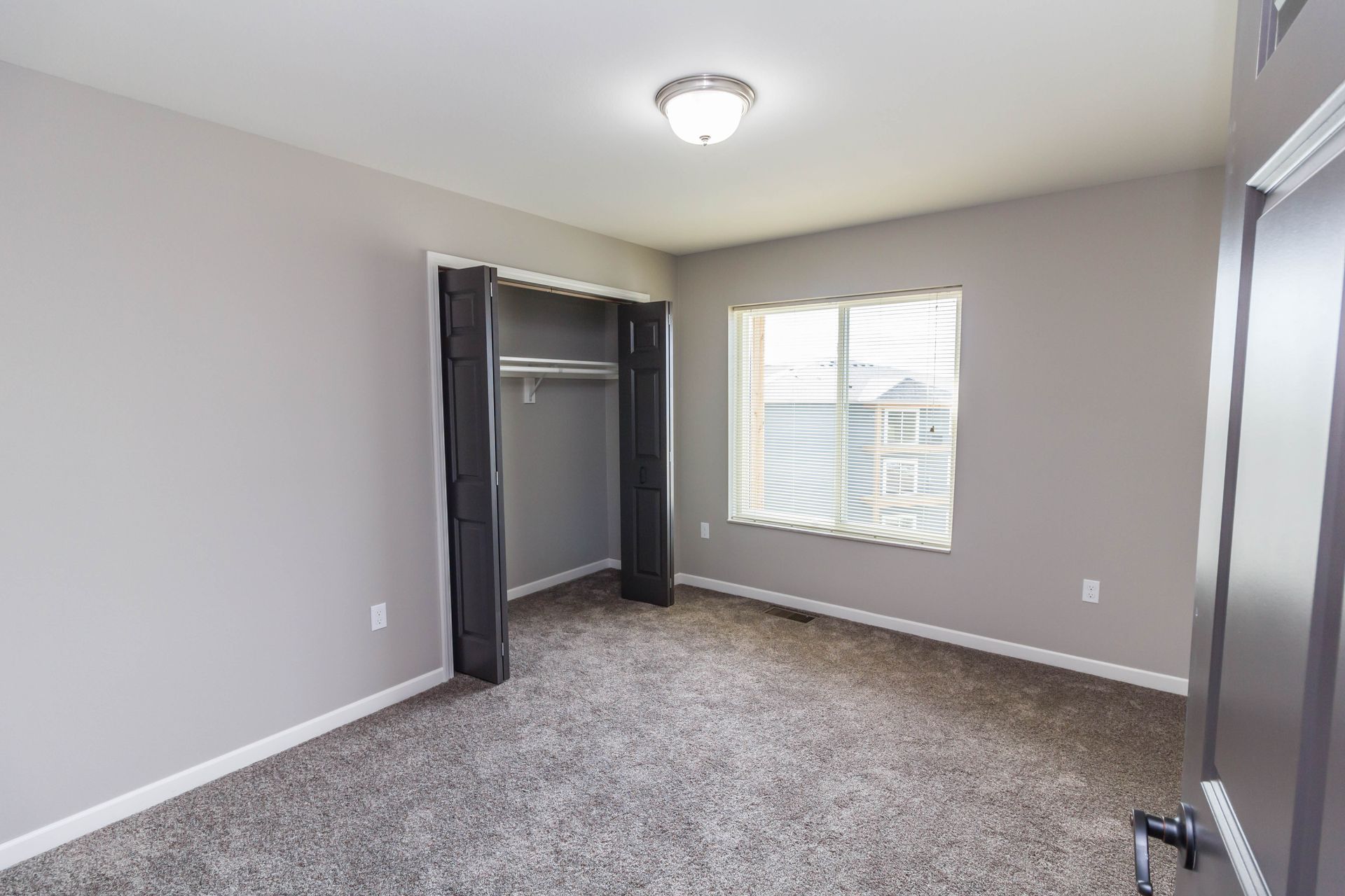 A bedroom with gray walls, carpet, and a closet. A window with blinds is on one wall.