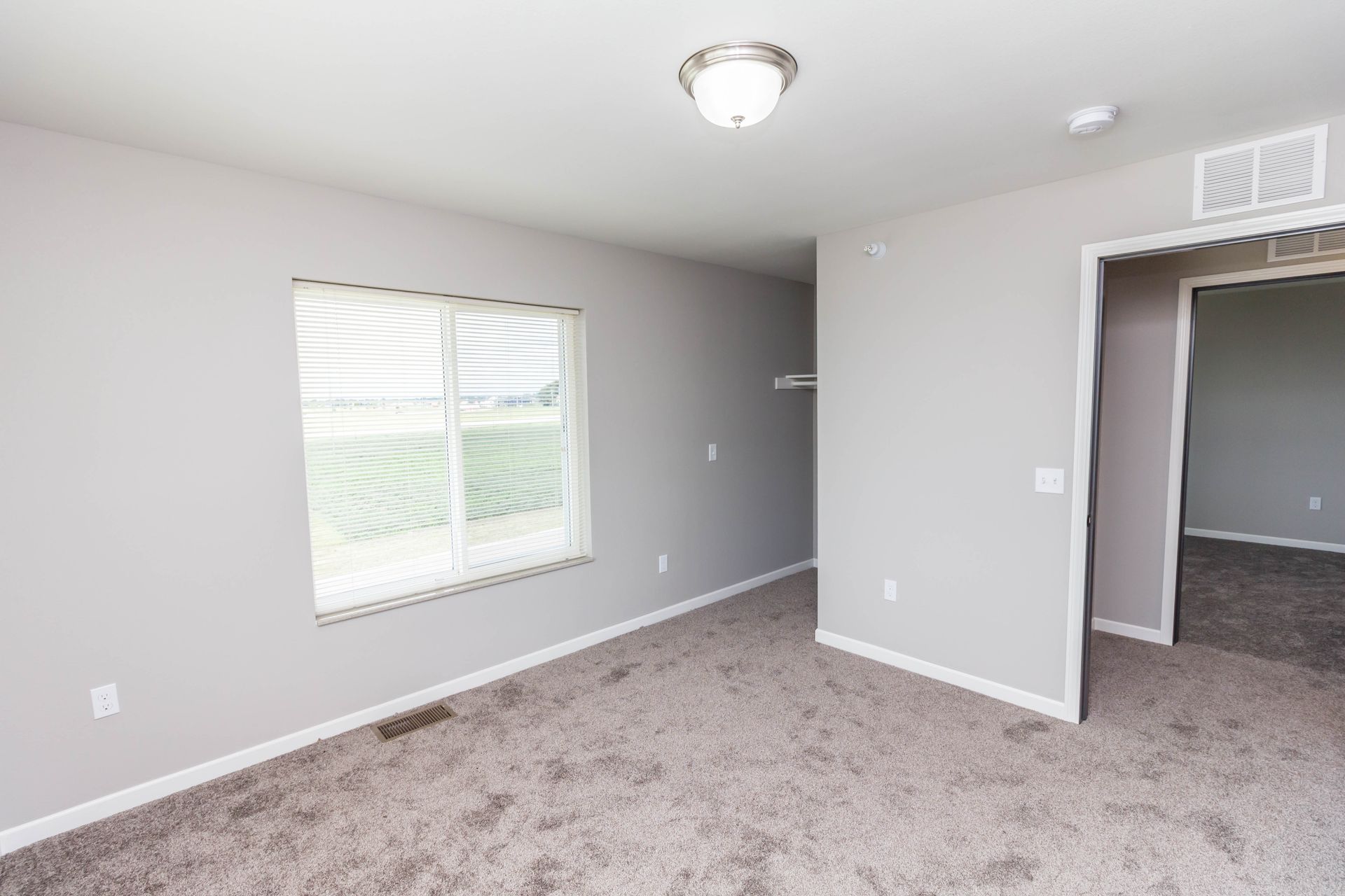 Empty bedroom with gray walls, carpet, window, and a doorway leading to another room.