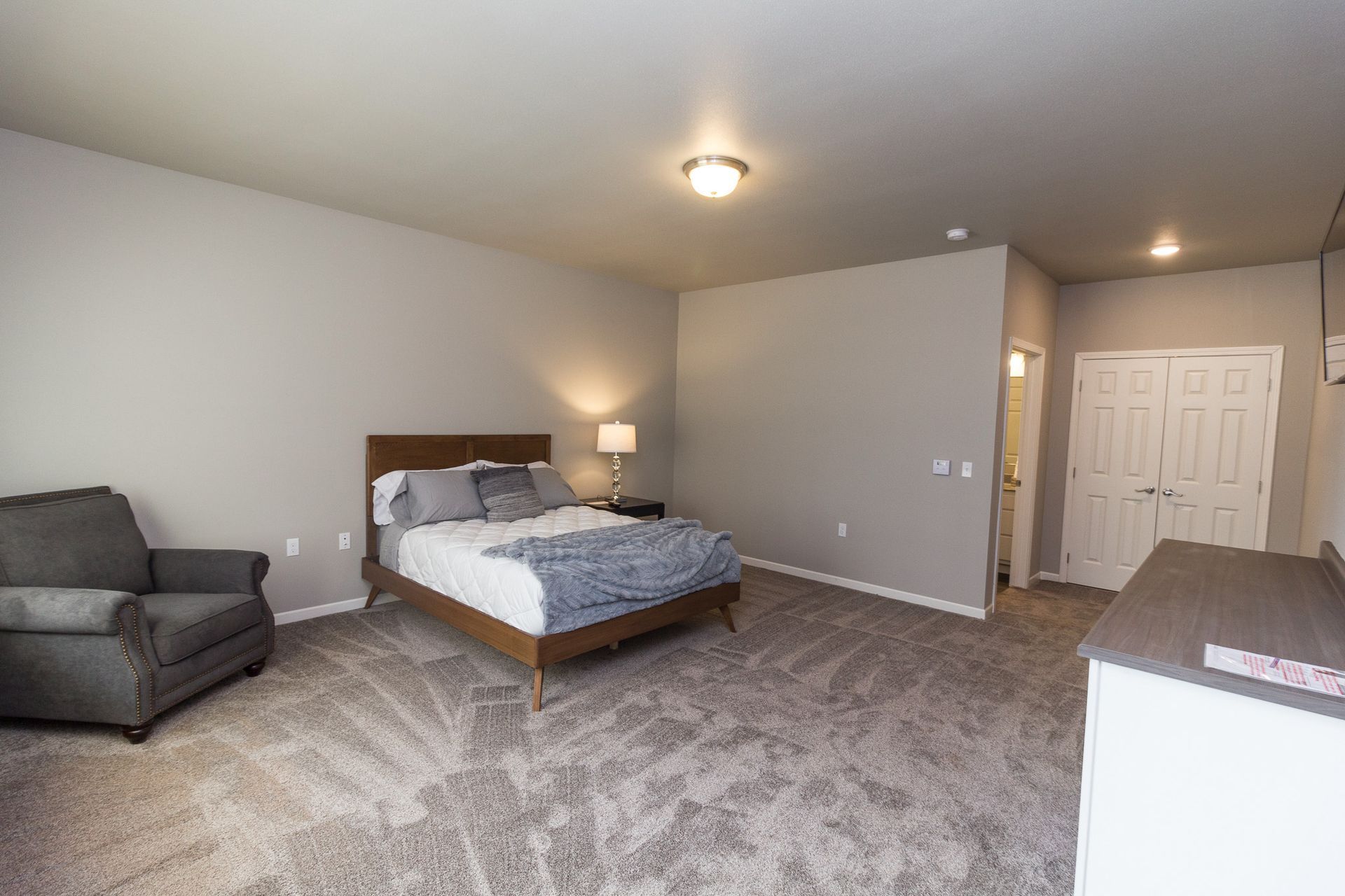 Bedroom with a bed, armchair, dresser, and closet. The room has neutral gray walls and carpet.