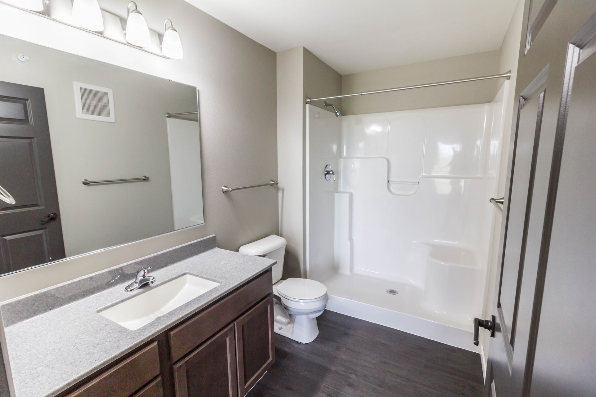 A modern bathroom with a dark wood vanity, gray walls, and a white shower stall. Dark wood floors and trim provide contrast.