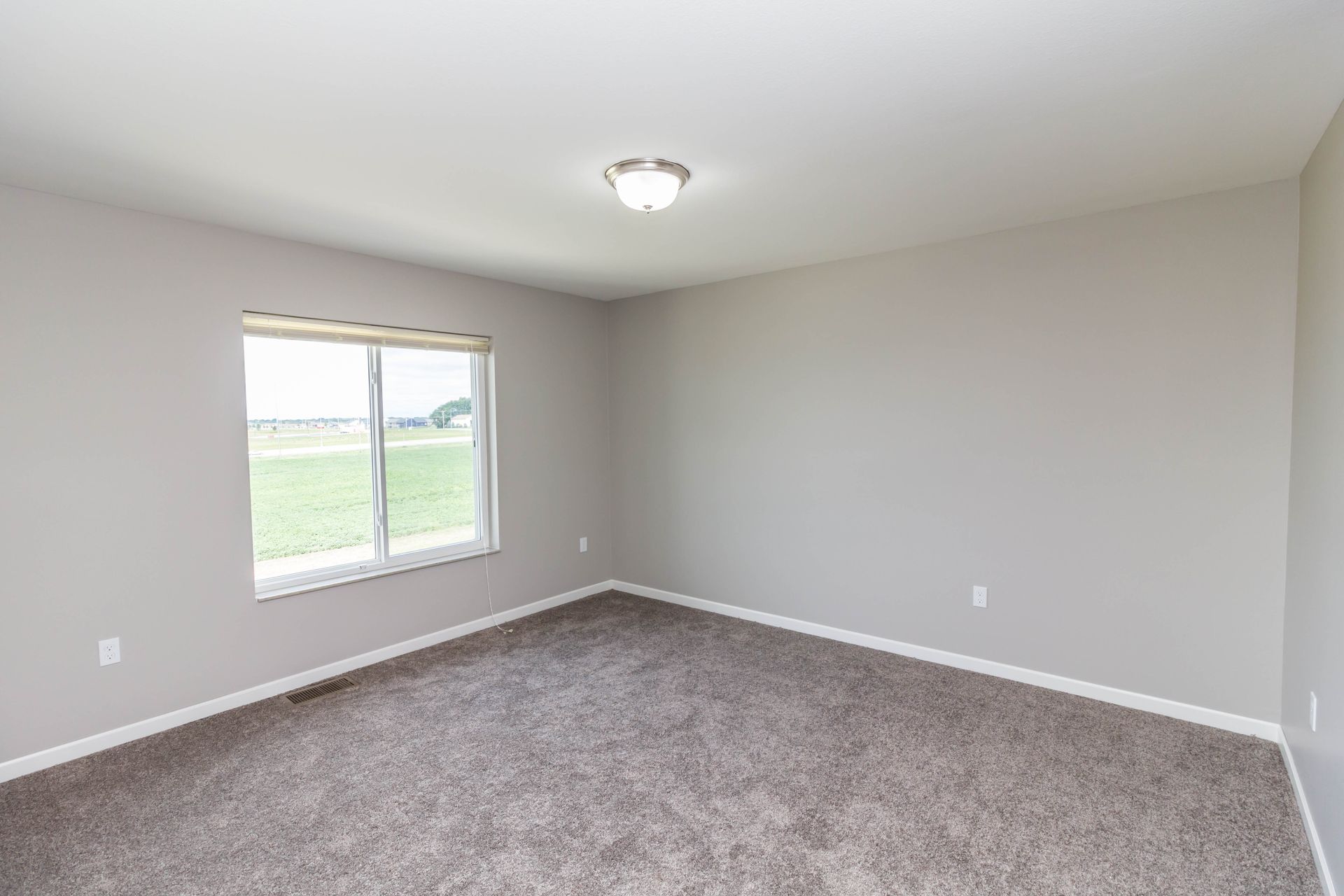 Empty bedroom with gray walls, brown carpet, a window, and a ceiling light.