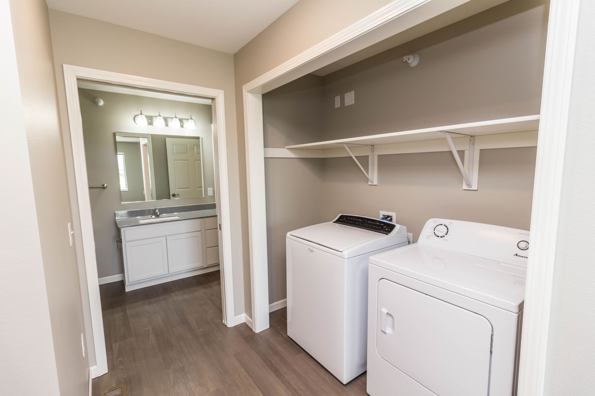 Laundry room with a white washer and dryer, shelves, and a doorway leading to a bathroom with a white vanity.