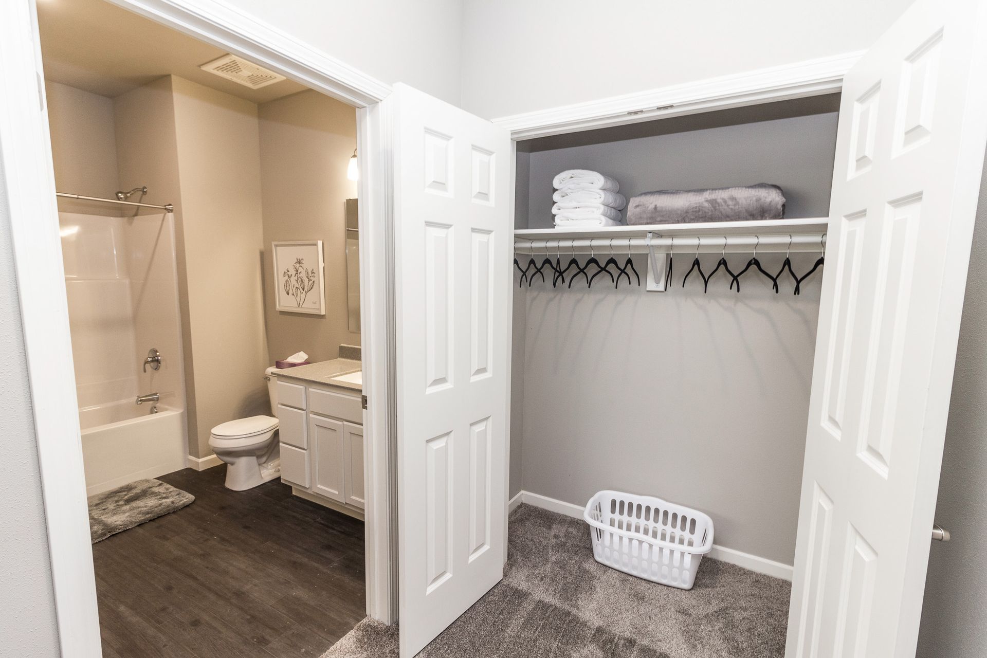 Bathroom and closet doorway. Bathroom has a tub/shower combo, toilet, and vanity. Closet has hanging space, shelves, and a laundry basket.
