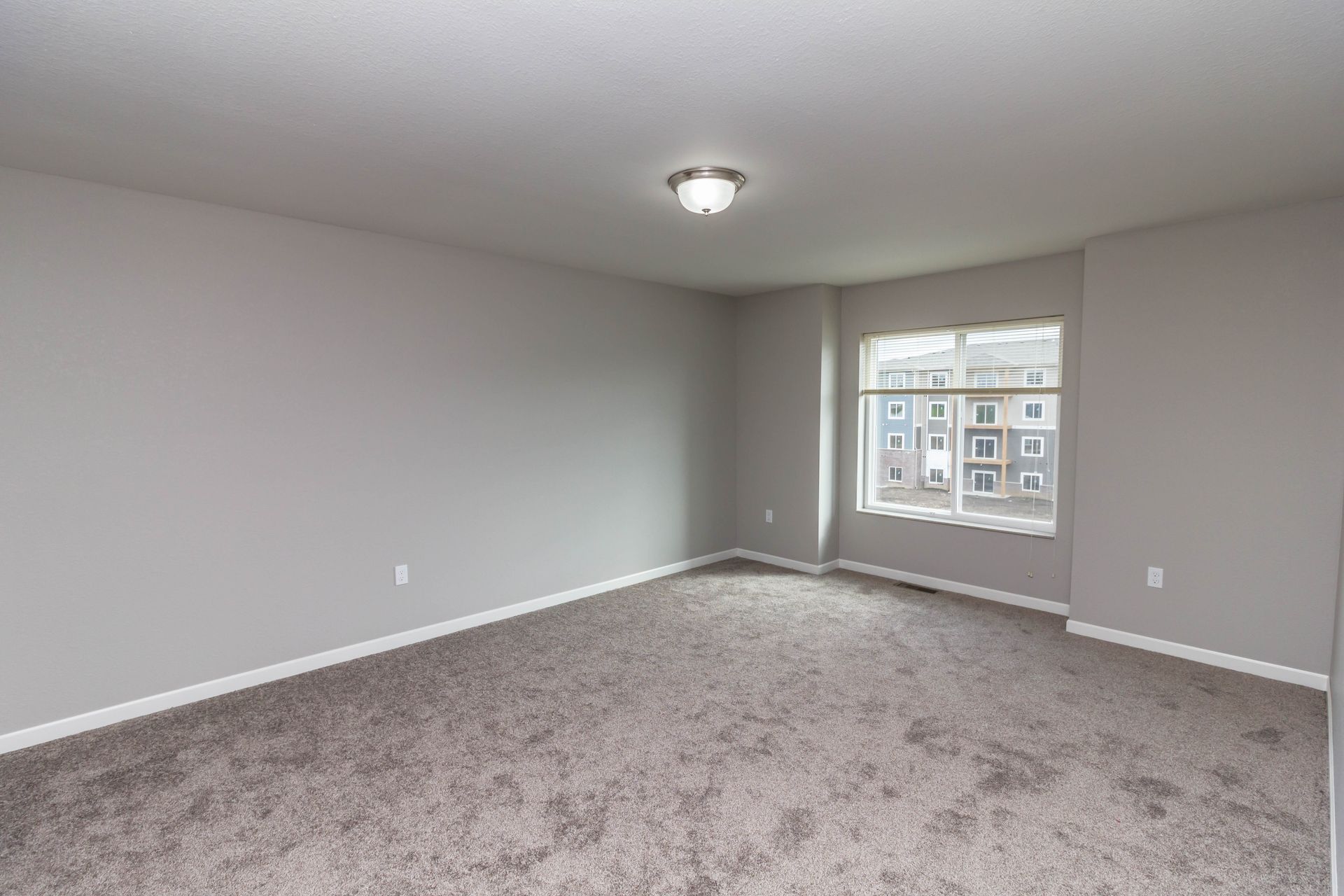 Empty room with gray walls and carpet, a small window, and a ceiling light.