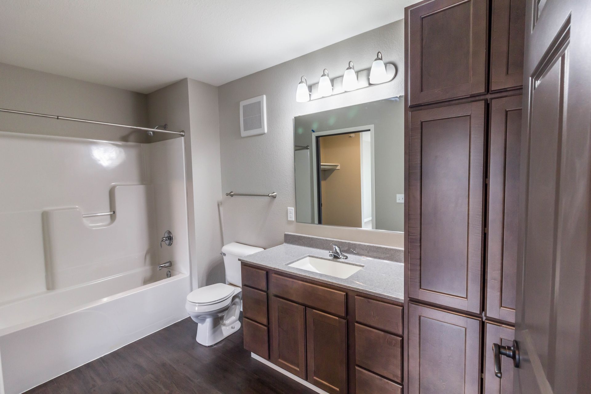 Bathroom with a white tub and toilet, dark brown cabinets, and a large mirror.