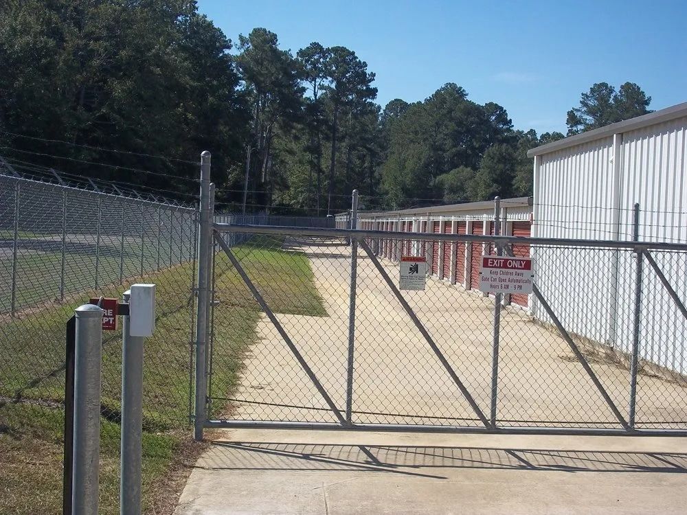 A gated storage facility with red doors, chain link fence, and concrete pathway.