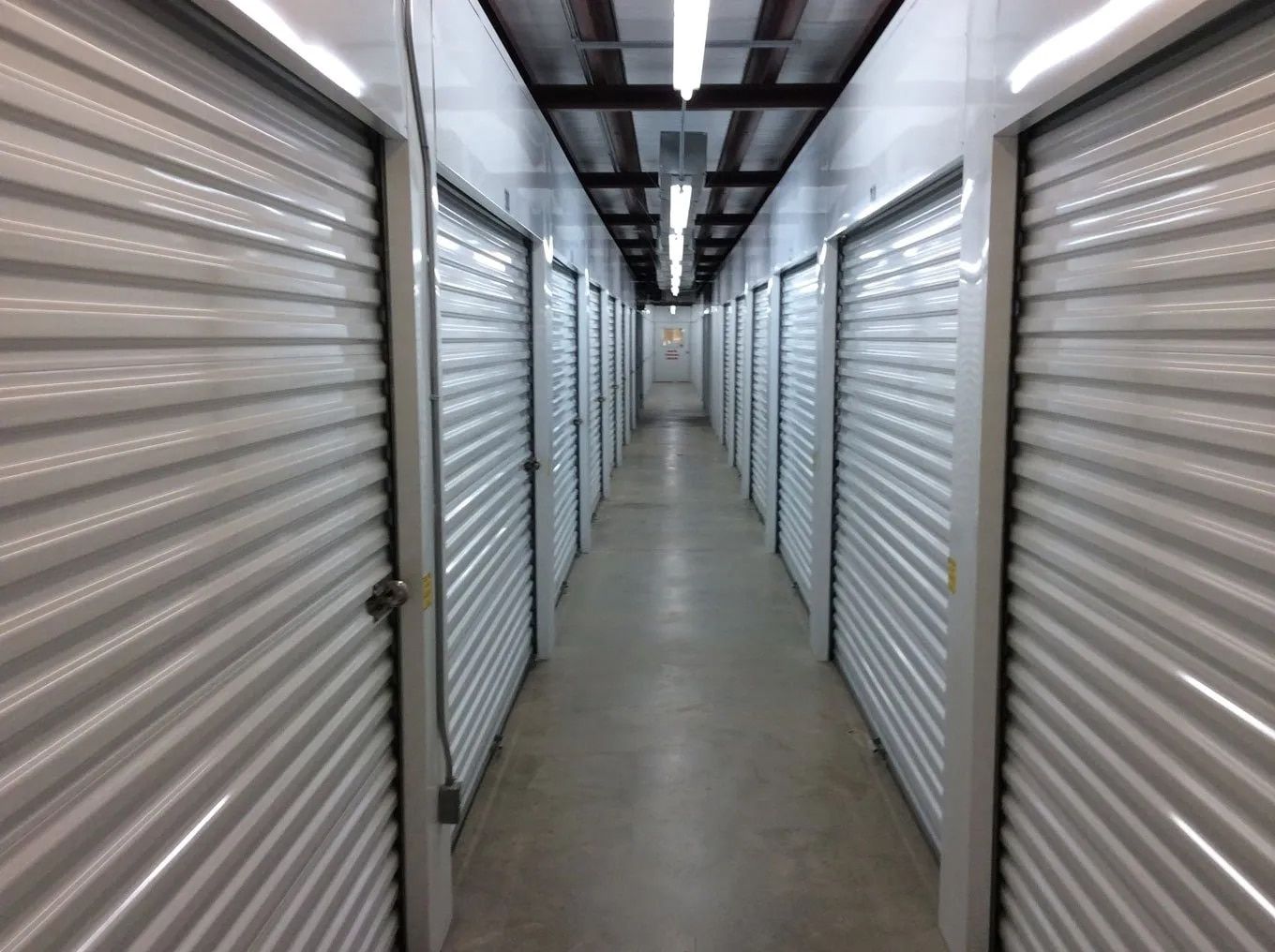 Hallway of self-storage units with closed, white doors and metal ceilings.