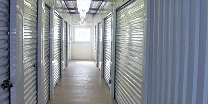 Interior of a storage unit facility hallway with units on either side; a window is visible at the end.