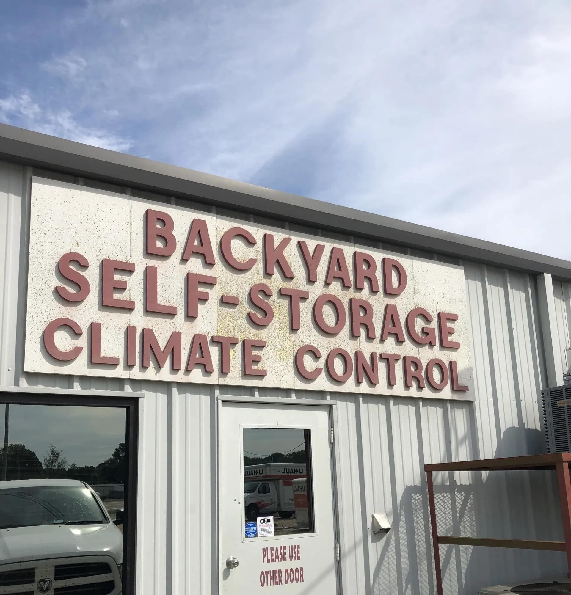 Sign for Backyard Self-Storage Climate Control; white building, red lettering, cloudy sky.