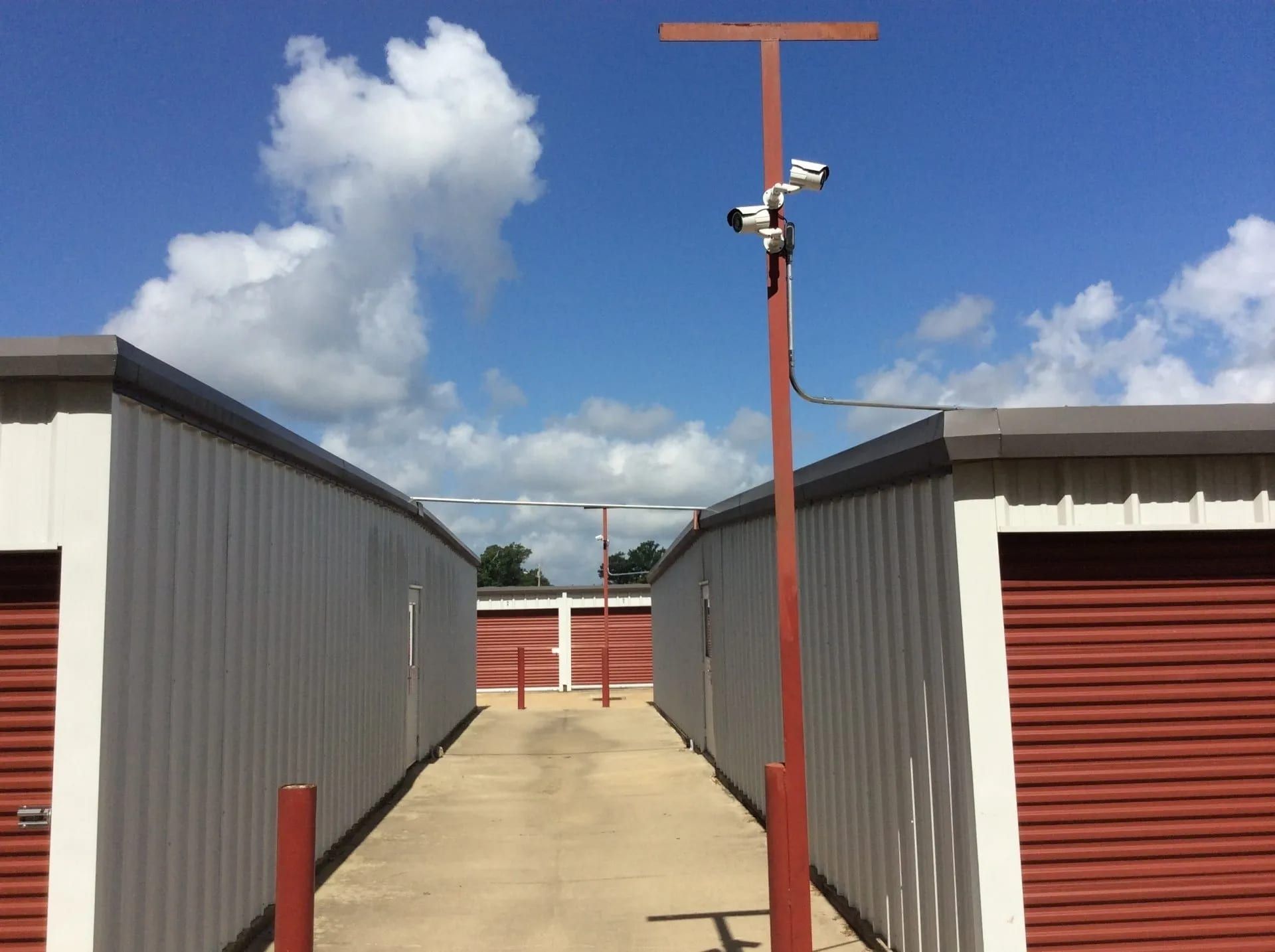 Storage units with red doors, a security camera pole, and a blue sky with clouds.