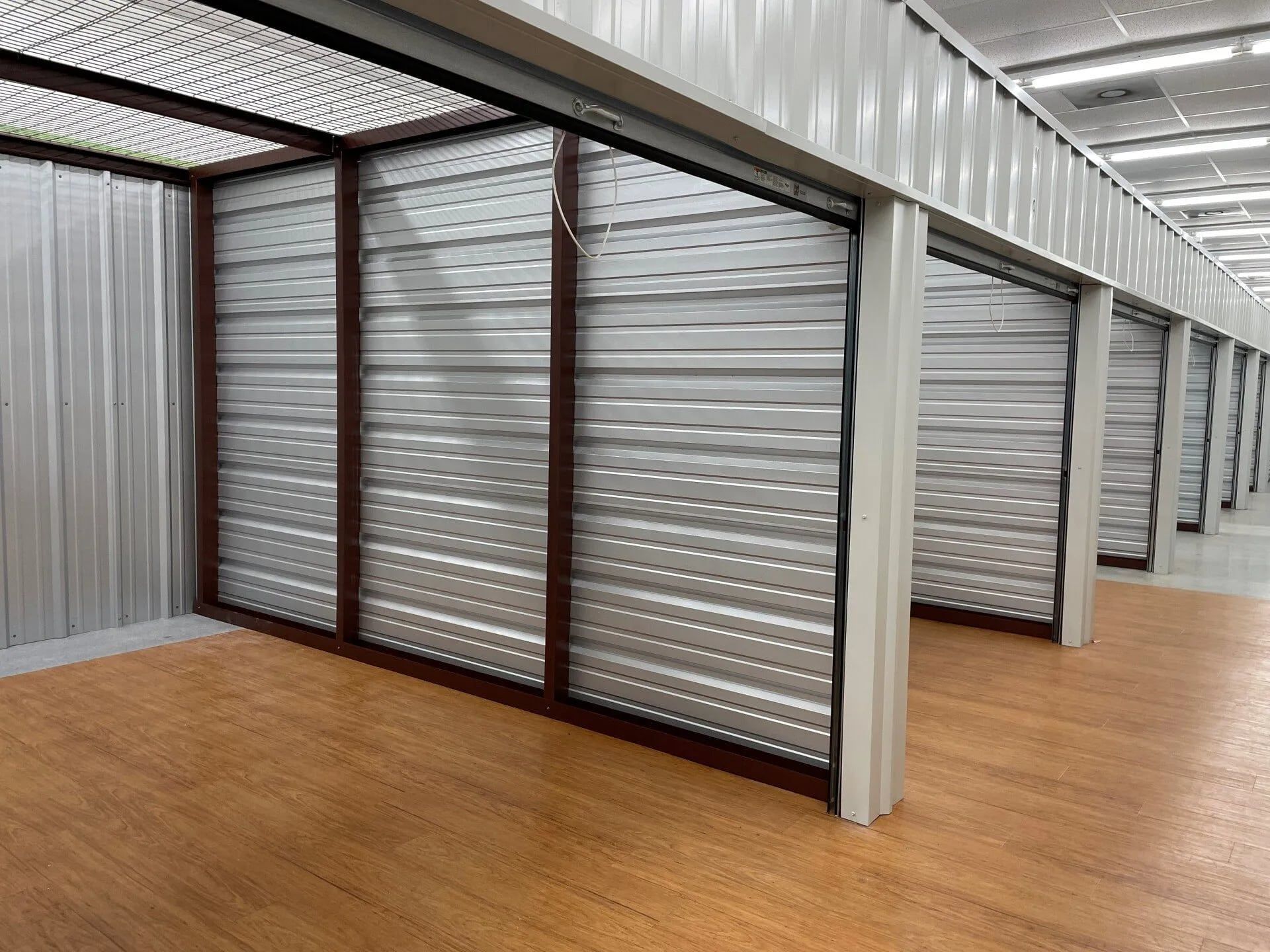 Interior view of storage units with metal walls, brown frames, and wood-like floors.