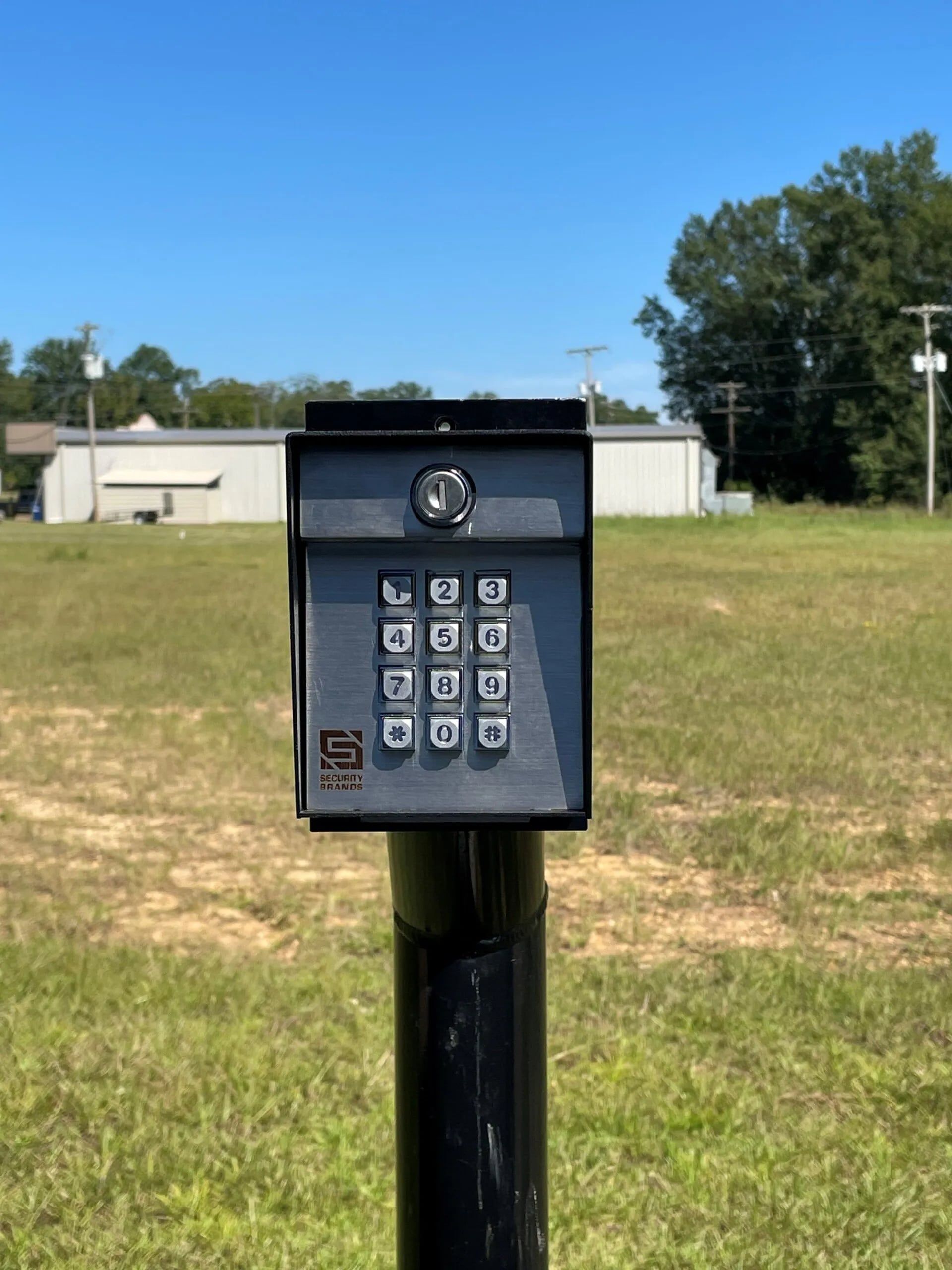 Black keypad on a pole in front of a building on a sunny day.
