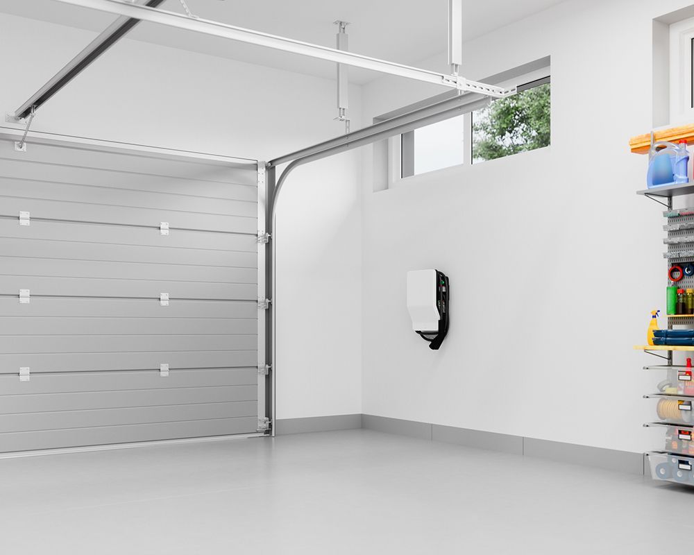 An empty garage with a garage door open and shelves filled with cleaning supplies.