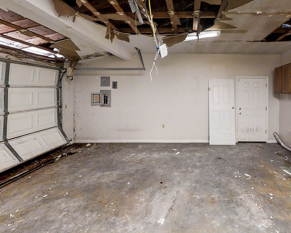 An empty garage with a garage door open and a broken ceiling.