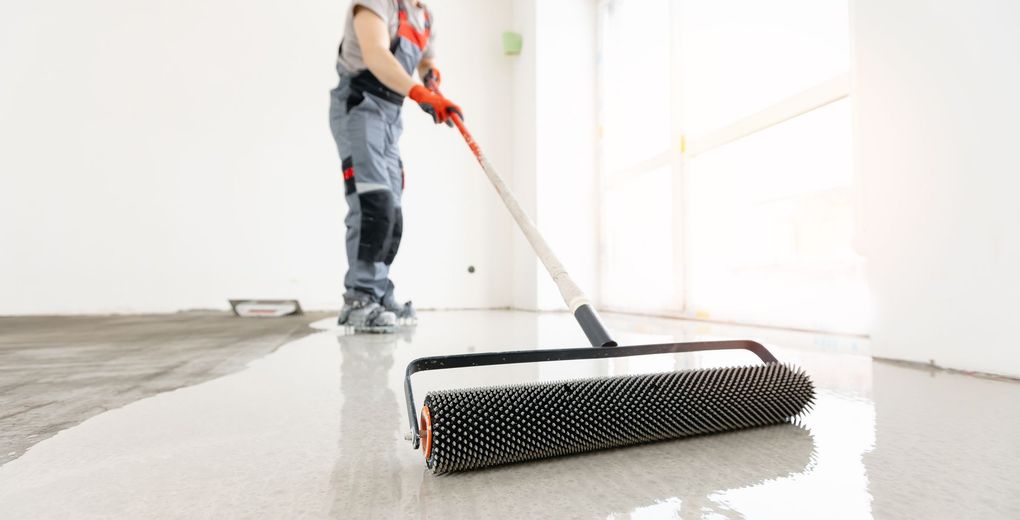 Person applying epoxy flooring with a spiked roller in an empty room.