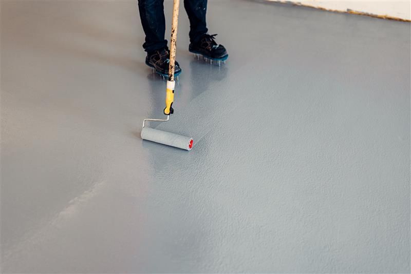 Person rolling gray epoxy coating on a concrete floor with a roller.