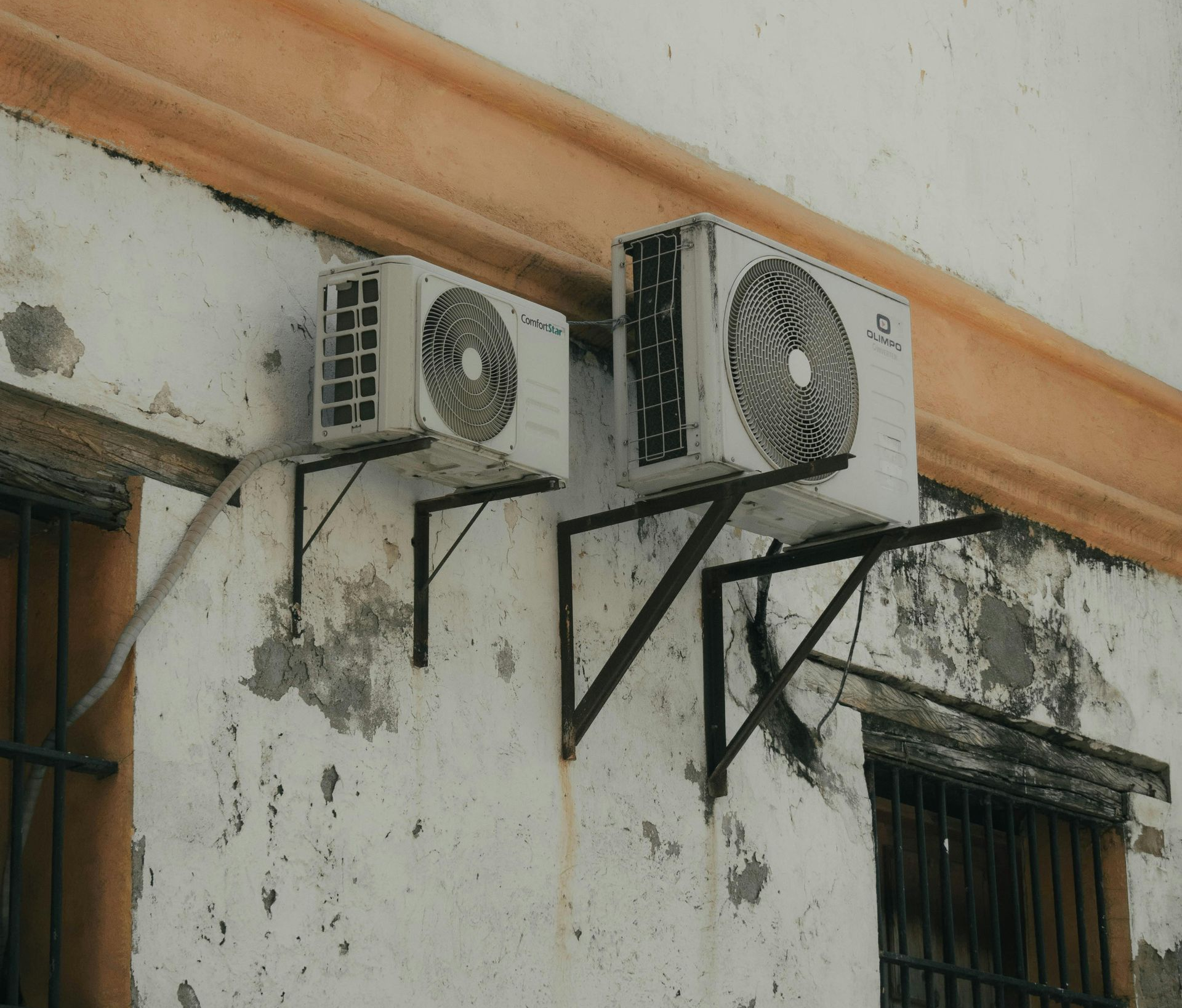 Two white air conditioning units mounted on an aged, weathered building wall.