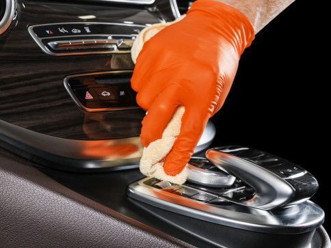 a person wearing orange gloves is cleaning the dashboard of a car .