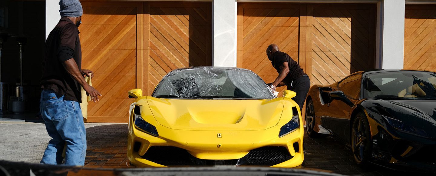 two men are washing a yellow sports car in front of a garage